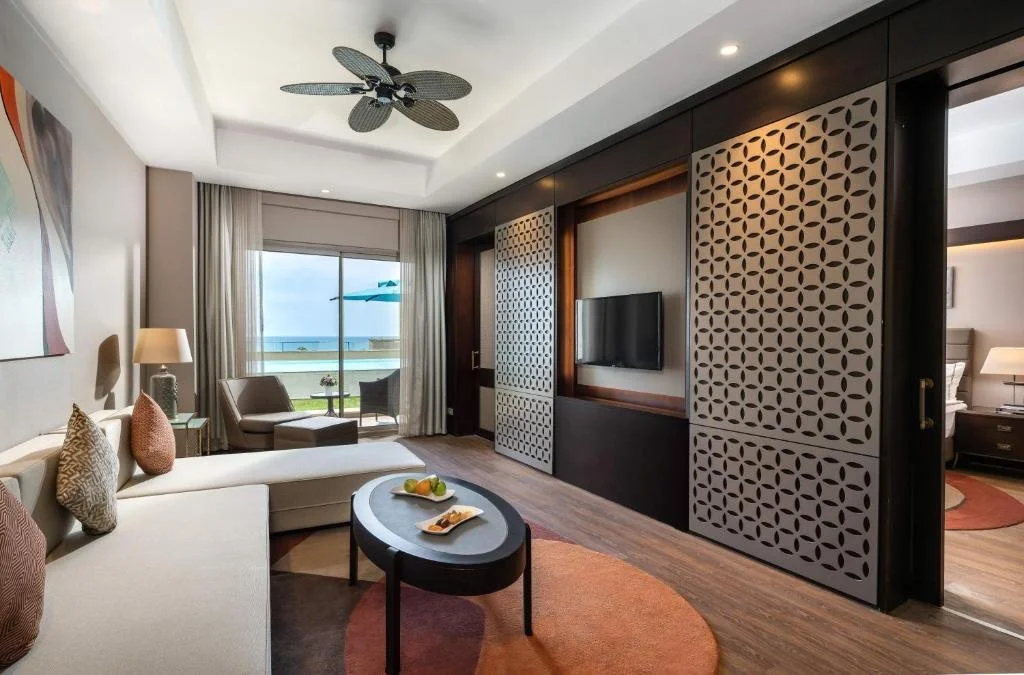 Kaya Palazzo Golf Resort Belek suite living area with sliding glass doors opening to a balcony with pool and sea view