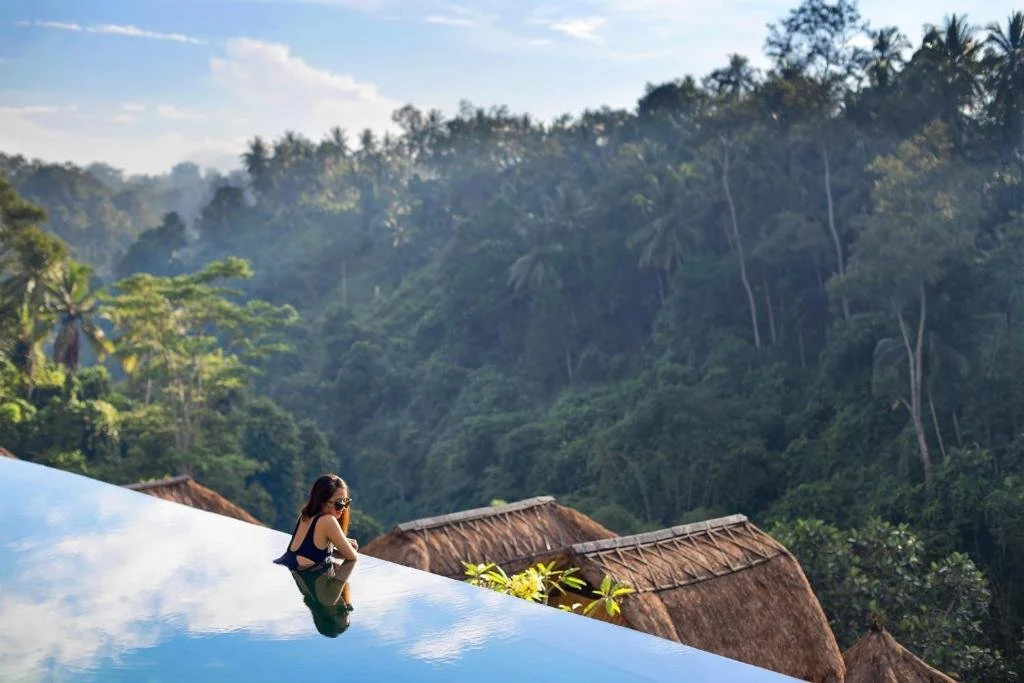 Viceroy Bali Ubud guest at infinity pool edge overlooking thatched bale villas and jungle canopy in the Valley of the Kings