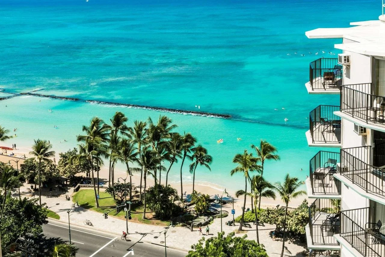 Aston Waikiki Beach Tower Honolulu balcony view over Kuhio Beach, rock breakwater, and turquoise Pacific