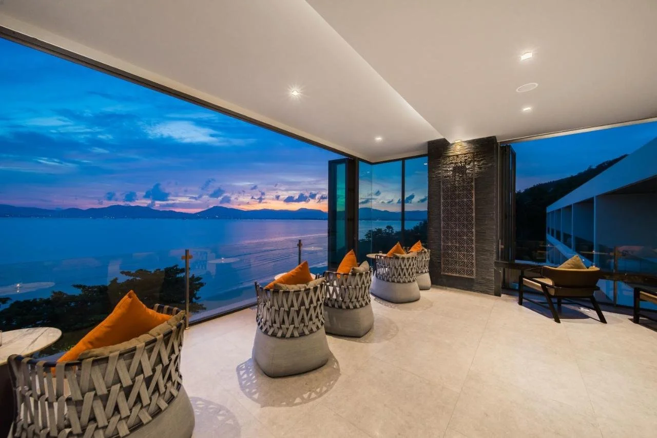 My Beach Resort Phuket terrace lounge at dusk with panoramic Andaman Sea and mountain silhouette through full-width glass wall