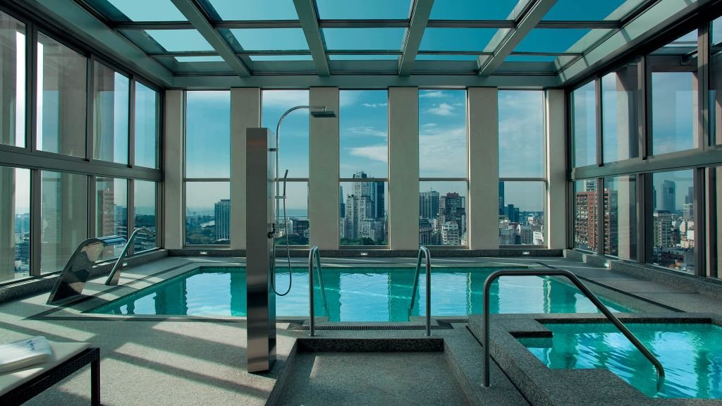 Alvear Art Hotel Buenos Aires rooftop indoor pool with retractable glass ceiling, stainless steel shower column, and city skyline through floor-to-ceiling windows