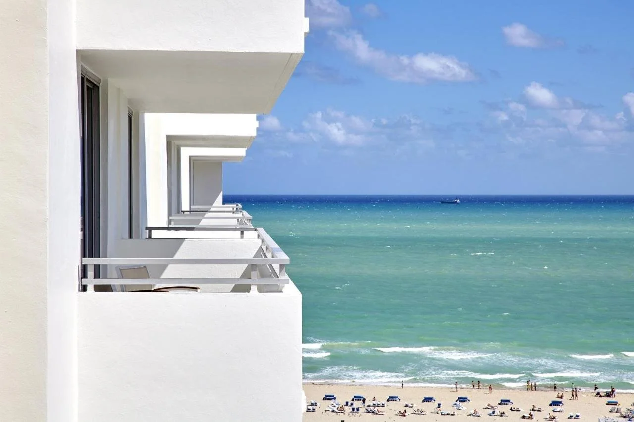 Loews Miami Beach Hotel South Beach stacked ocean-facing balconies with Atlantic Ocean, sandy beach and blue umbrellas below