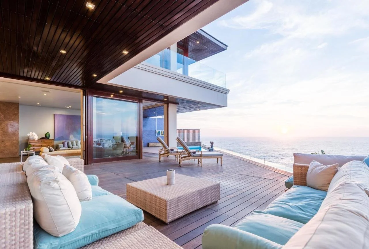 Ellerman House Cape Town ocean-facing terrace with outdoor living area and upper-floor balcony overlooking the Atlantic Ocean at dusk from Bantry Bay