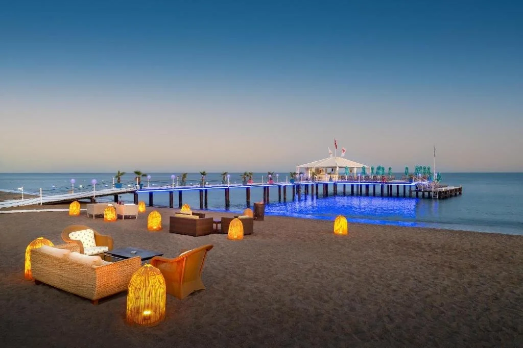 Concorde De Luxe Resort Antalya illuminated beachfront pier at dusk with lantern-lit lounge seating on the sand