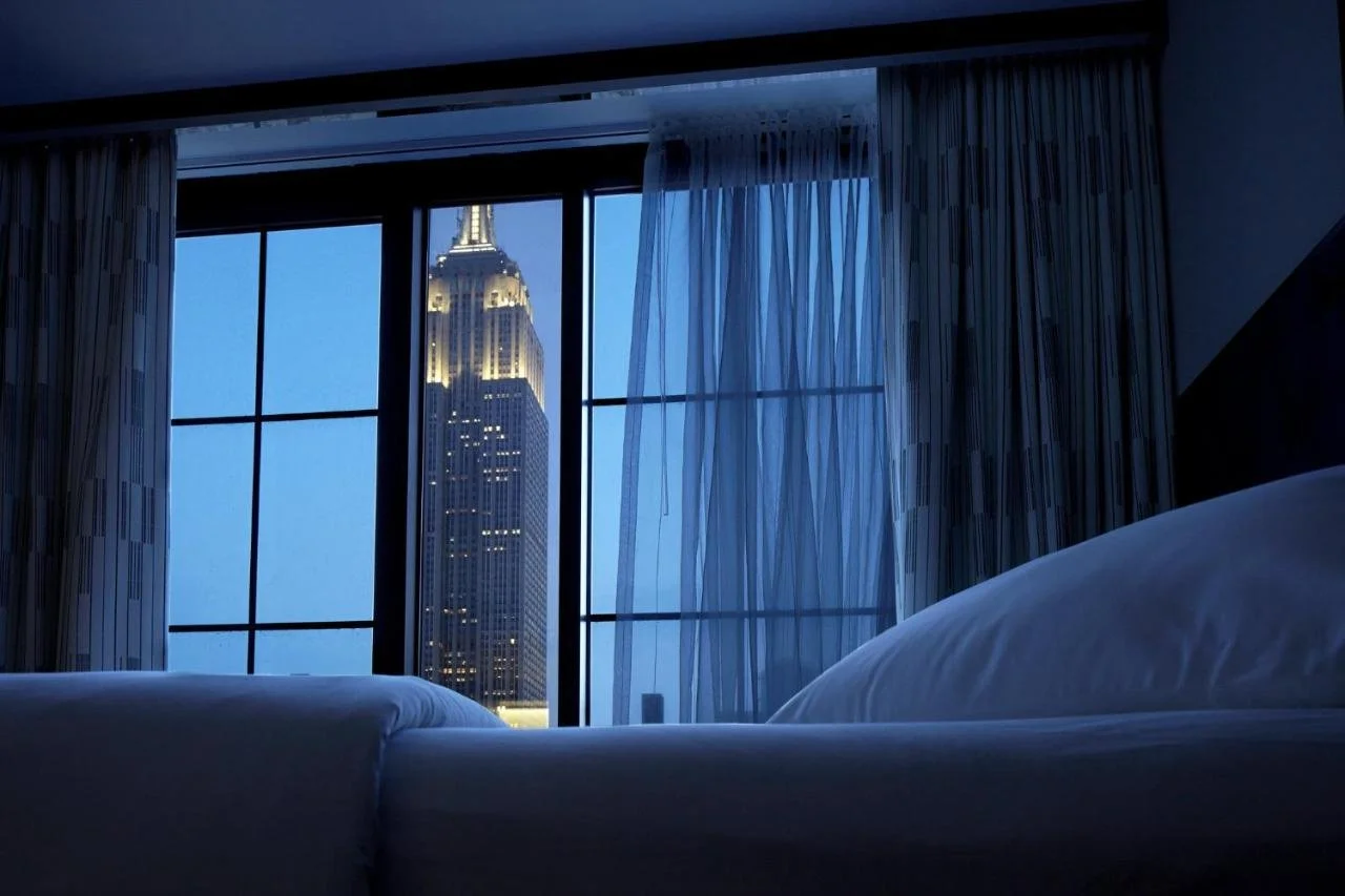 Archer Hotel New York room at dusk with illuminated Empire State Building through floor-to-ceiling windows