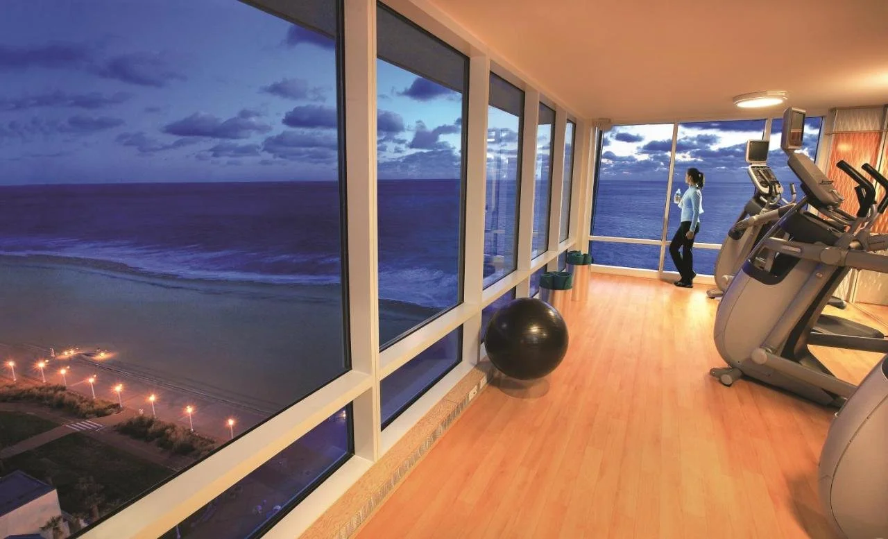 Hilton Vacation Club Ocean Beach Club Virginia Beach high-floor fitness center with floor-to-ceiling windows and panoramic ocean view at dusk