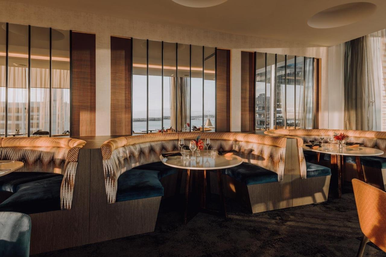 Mövenpick Hotel Auckland Auckland BODA restaurant curved upholstered booth seating with floor-to-ceiling windows and a harbour view through sheer curtains