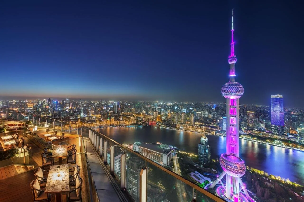 The Ritz-Carlton Shanghai Pudong FLAIR rooftop terrace at night with Oriental Pearl Tower illuminated in pink at close range and the Bund below