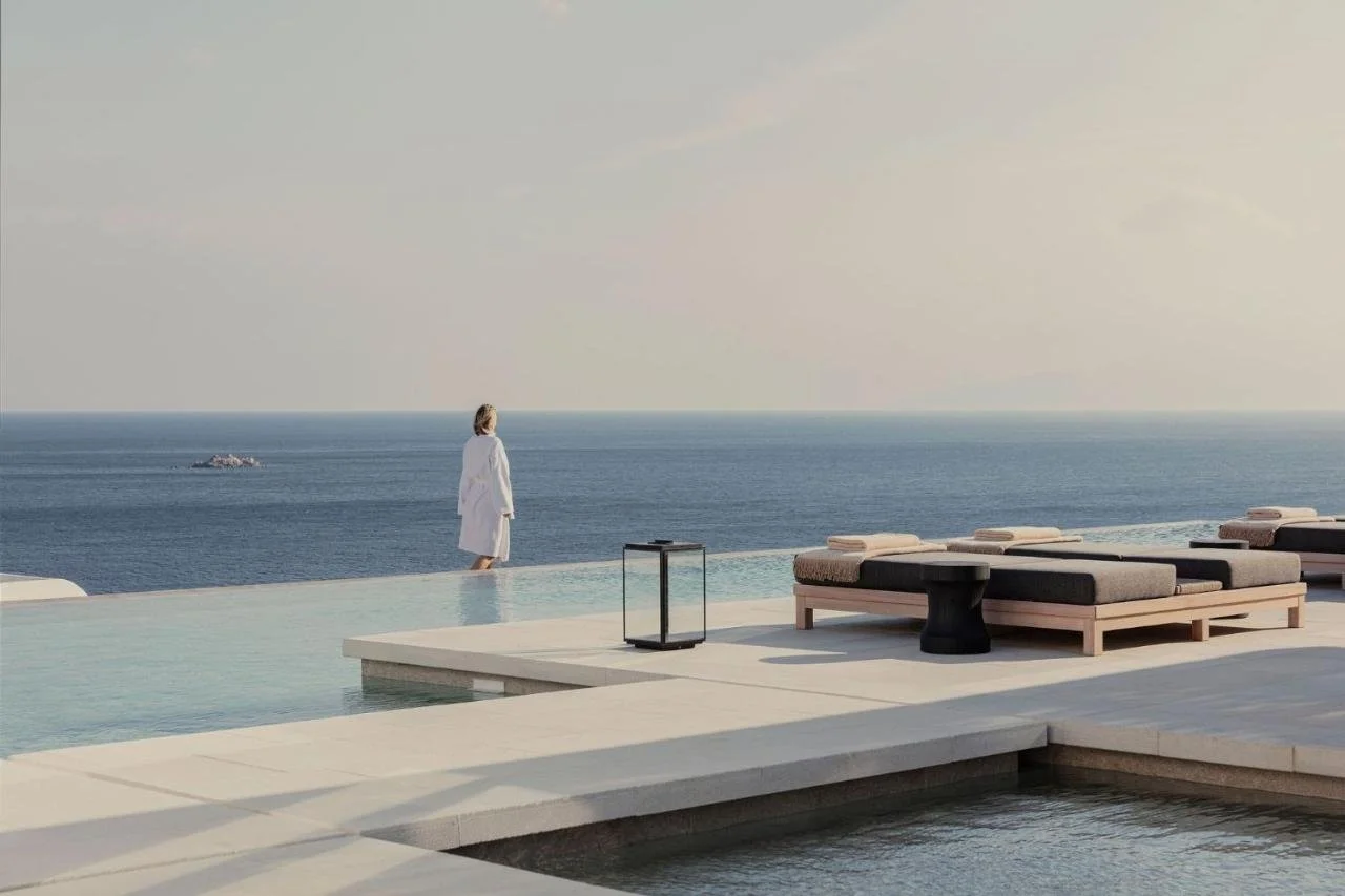 Kalesma Mykonos infinity pool terrace at dawn with guest in bathrobe at pool edge facing open Aegean Sea horizon