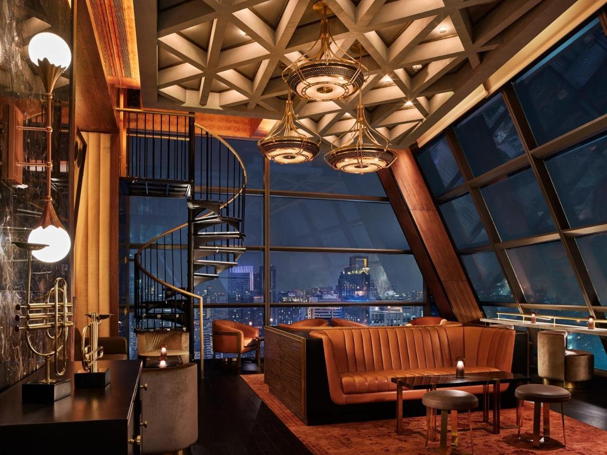 Rosewood Bangkok Lennon's bar interior with spiral staircase amber velvet seating and Bangkok city lights at night