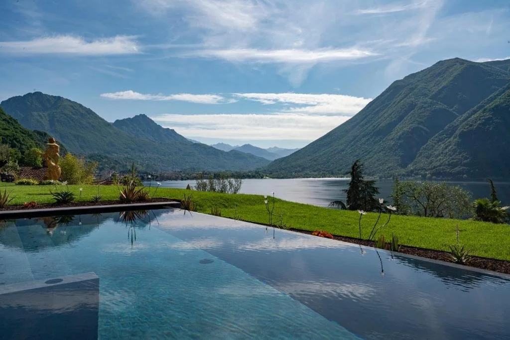 ARIA Retreat & Spa Lake Lugano infinity pool overlooking the lake framed by two forested mountains with lush garden in the foreground