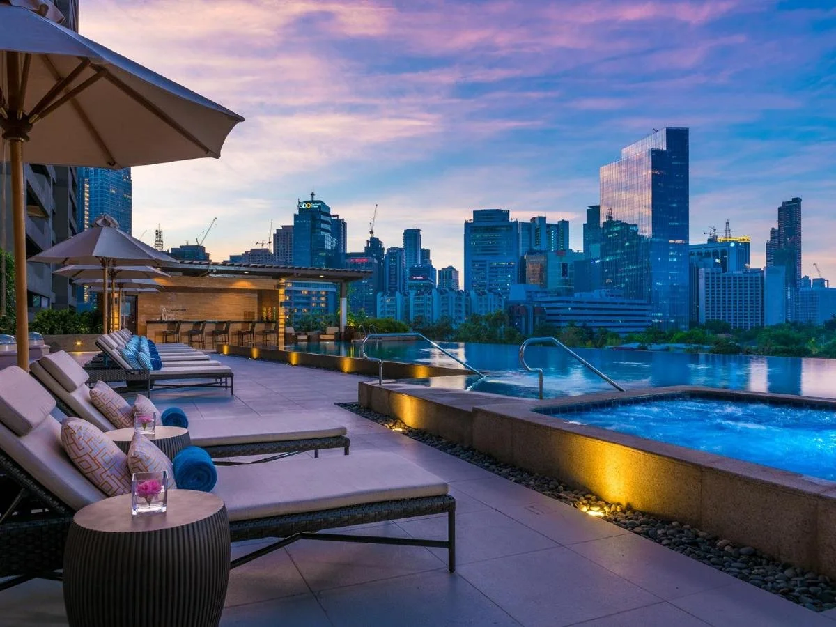 Discovery Primea Manila rooftop infinity pool deck with sunloungers and jacuzzi at sunset overlooking the Makati CBD skyline