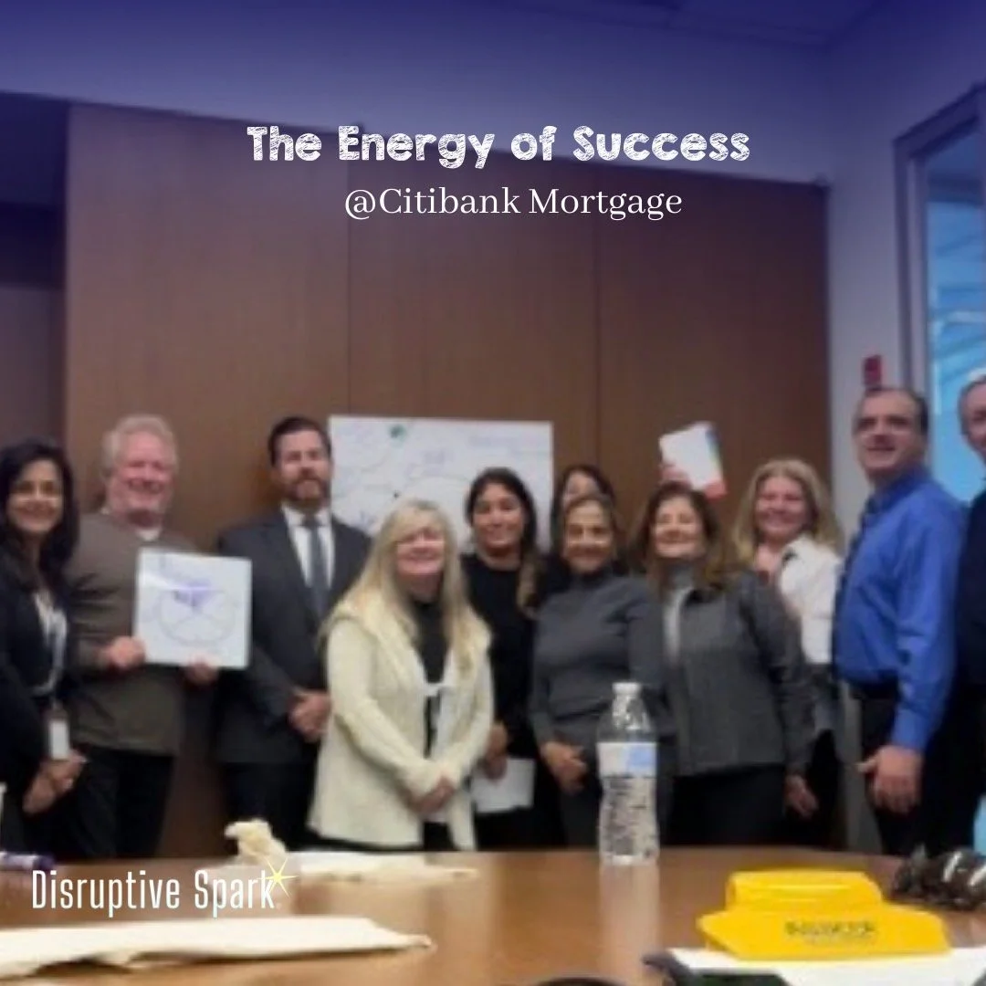 Group of professionals in a meeting room celebrating success, with a sign in the background that reads 'The Energy of Success' and '@Citibank Mortgage' at the top.