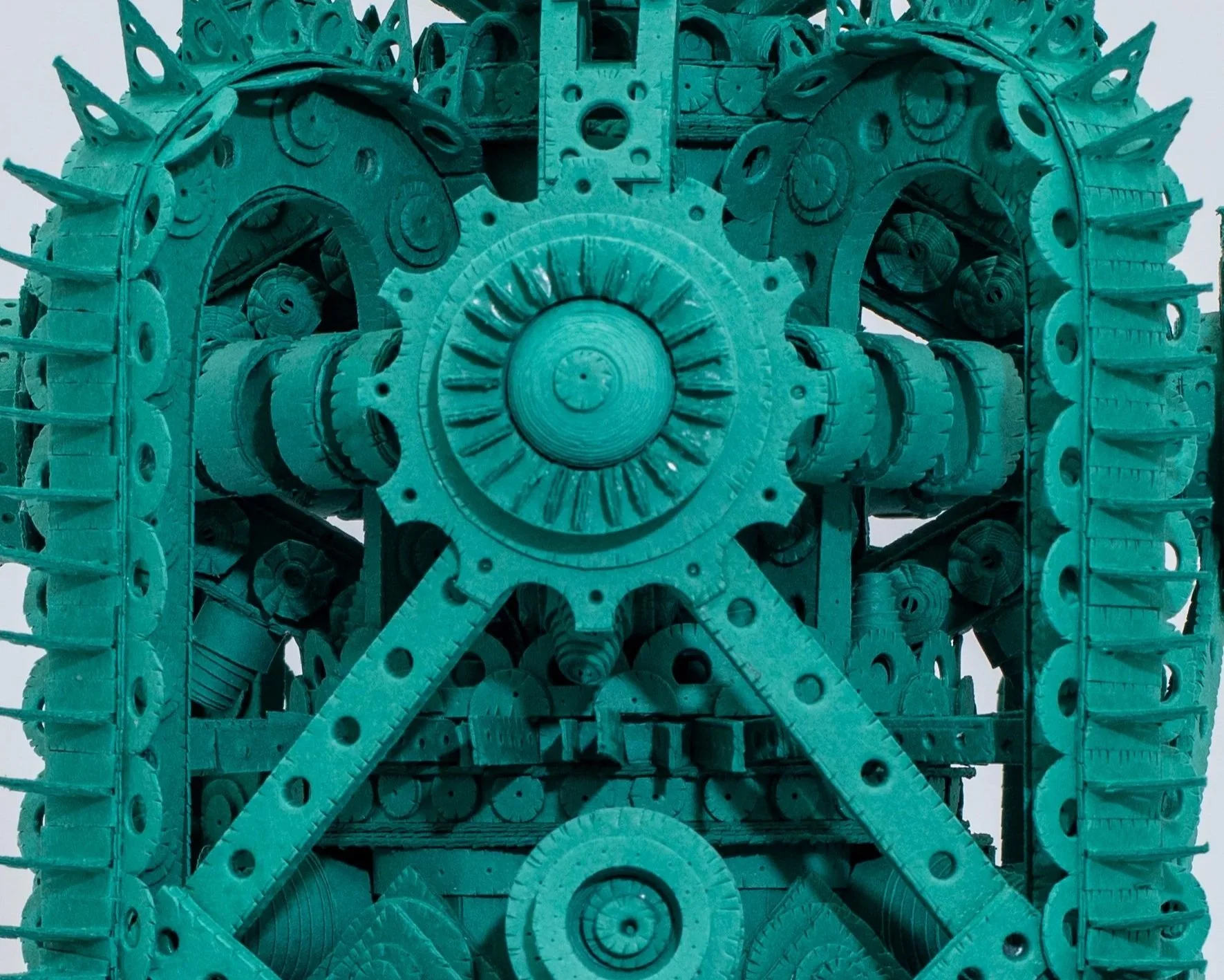 Close-up of a large, intricate, machine-like sculpture made of teal-colored wooden pieces, gears, and mechanical parts arranged in a symmetrical, complex pattern.