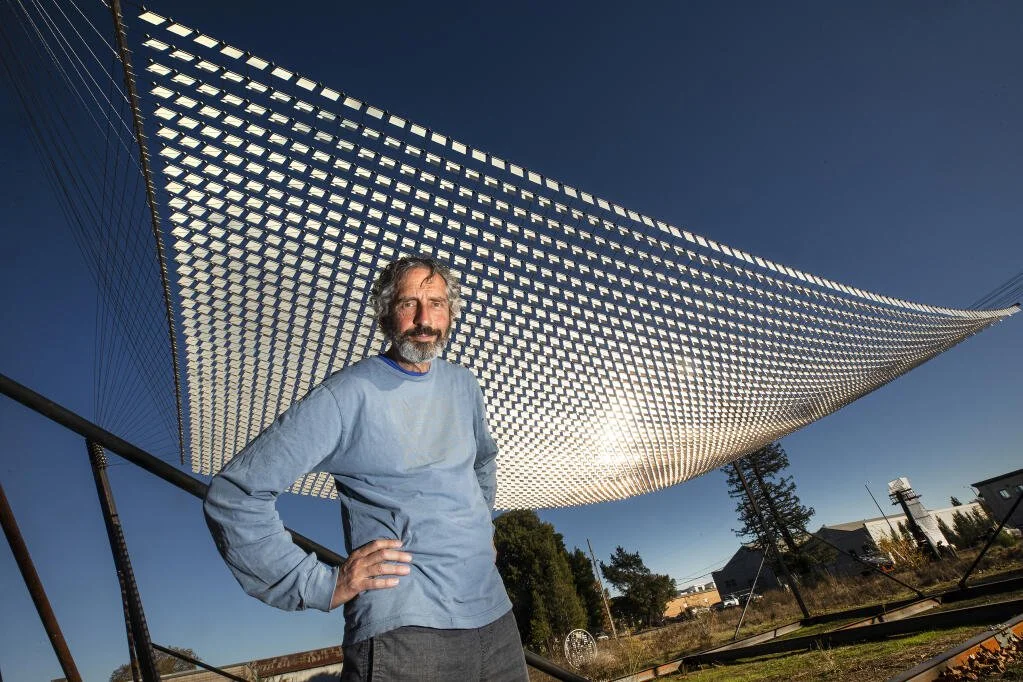 Man standing with a large reflective array in a field on a sunny day.