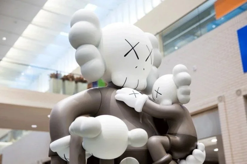 Large gray and white sculpture resembling a cartoon character hugging a smaller similar character in a shopping mall.