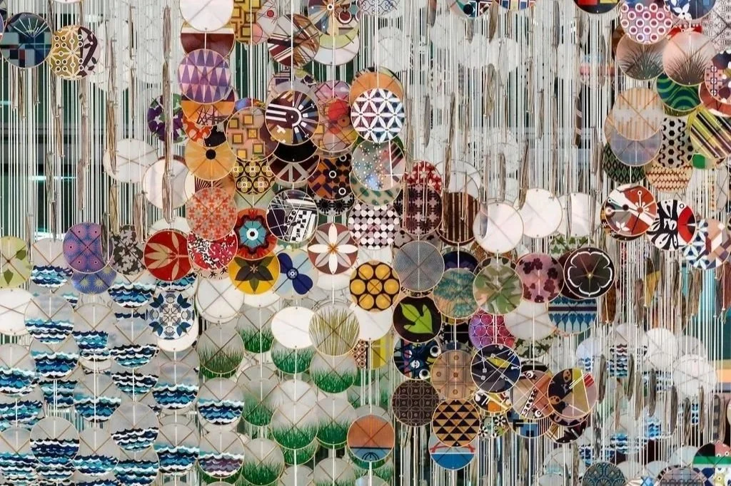 Colorful circular ornaments with various patterns hanging from thin strings, forming a large decorative display.