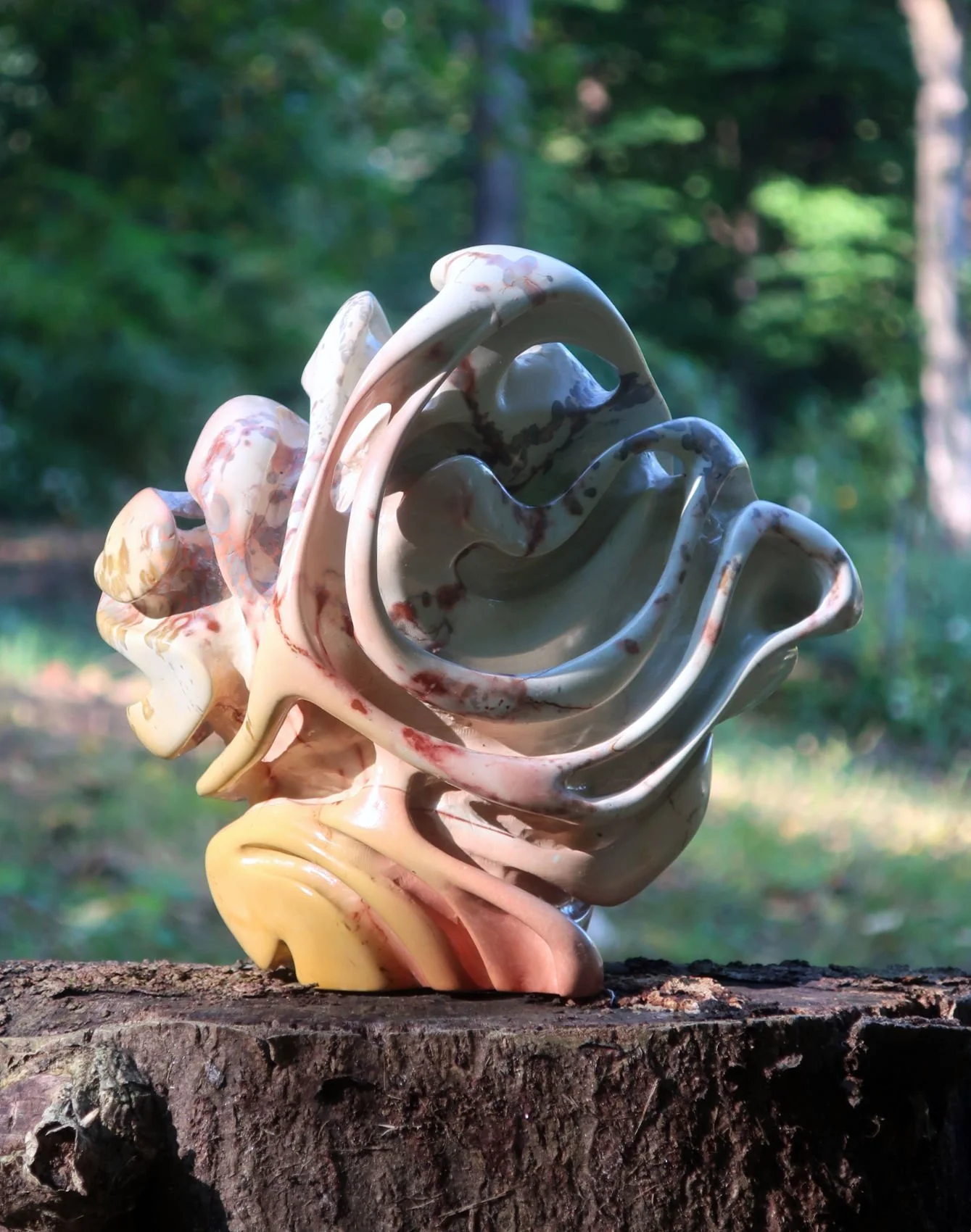 A marble sculpture resembling a rose flower, placed on a tree stump in a wooded outdoor setting.