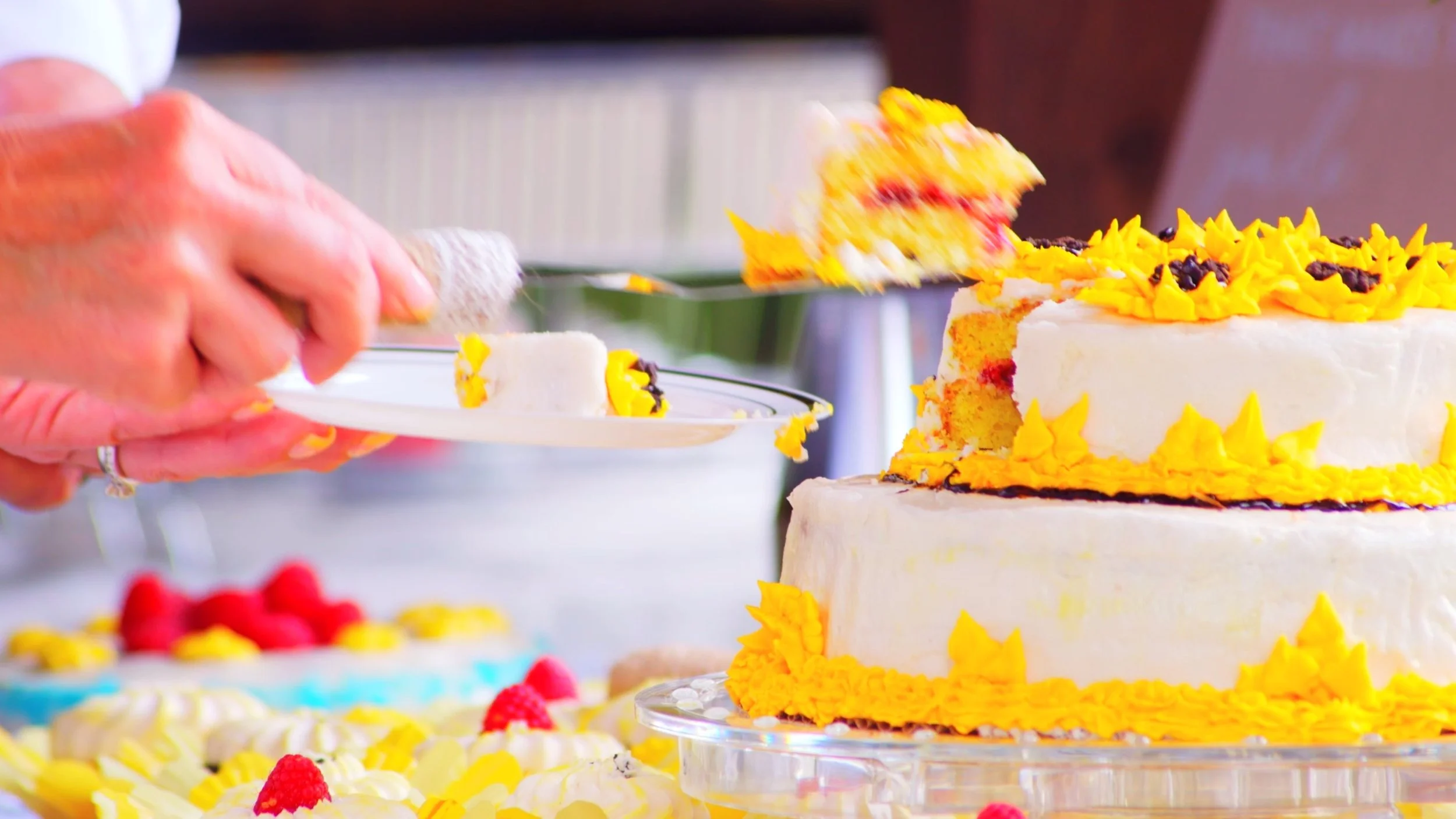 Person cutting a multi-layered cake decorated with yellow frosting and black accents, with a slice being served onto a plate.