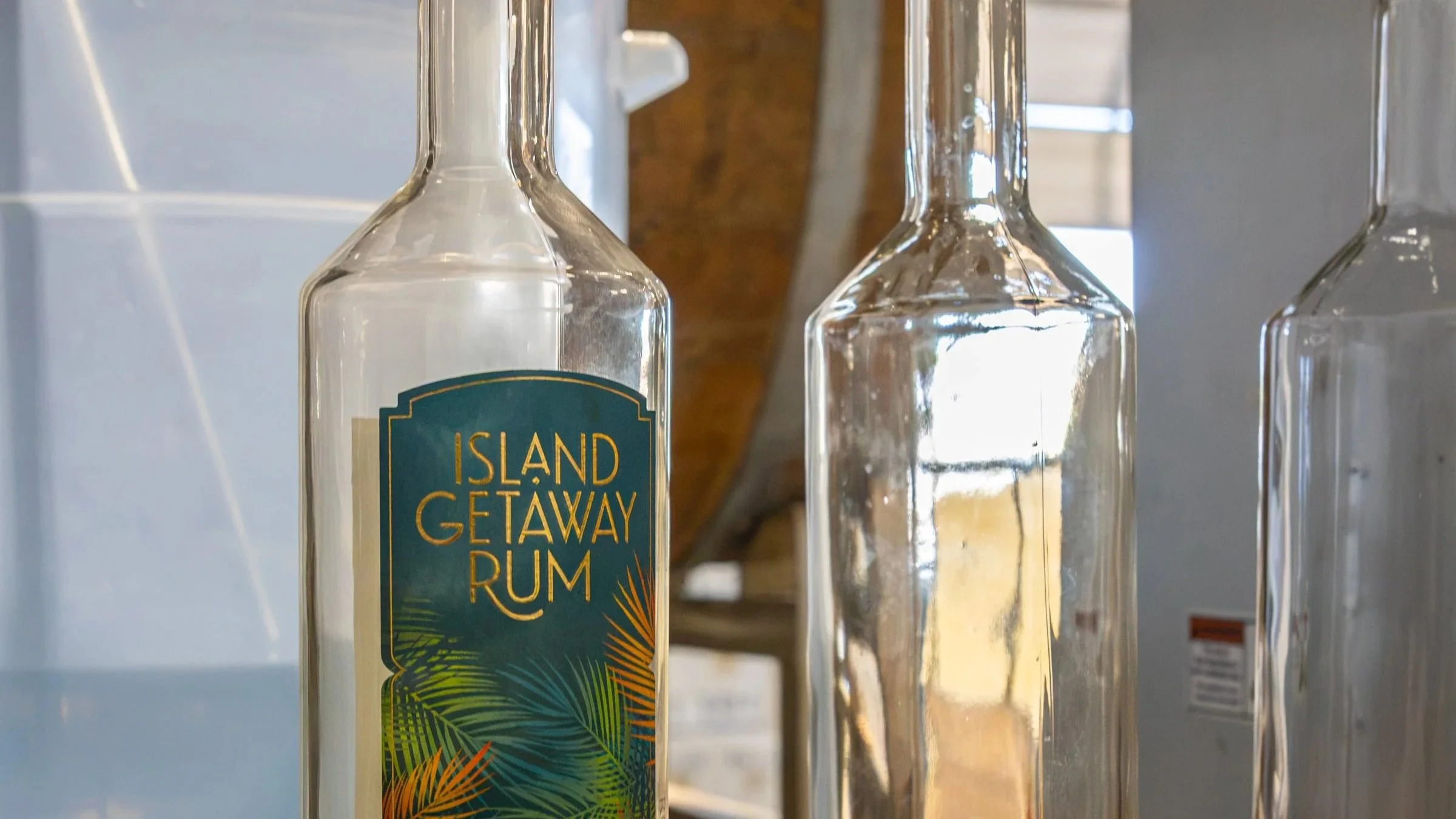 A clear glass bottle of Island Getaway Navy Rum with a colorful tropical palm design on the label, surrounded by other empty glass bottles, in a setting that resembles a bar or restaurant.