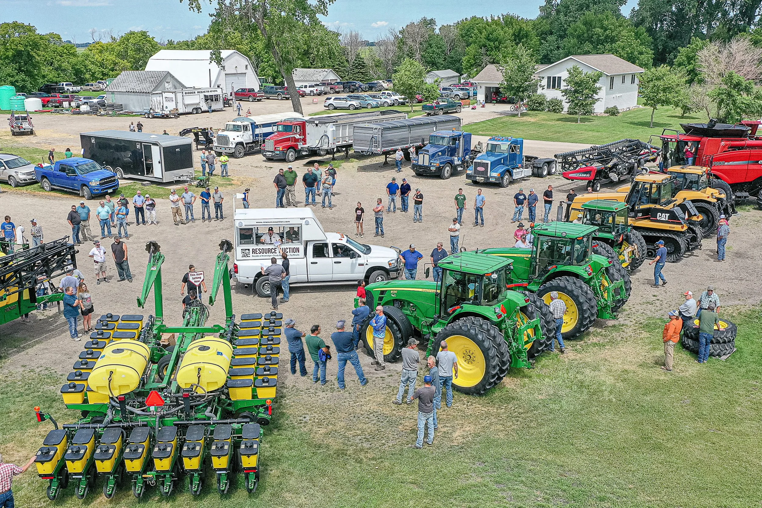 A large group of people gathering among rows of tractors and other farm equipment at an outdoor auction.