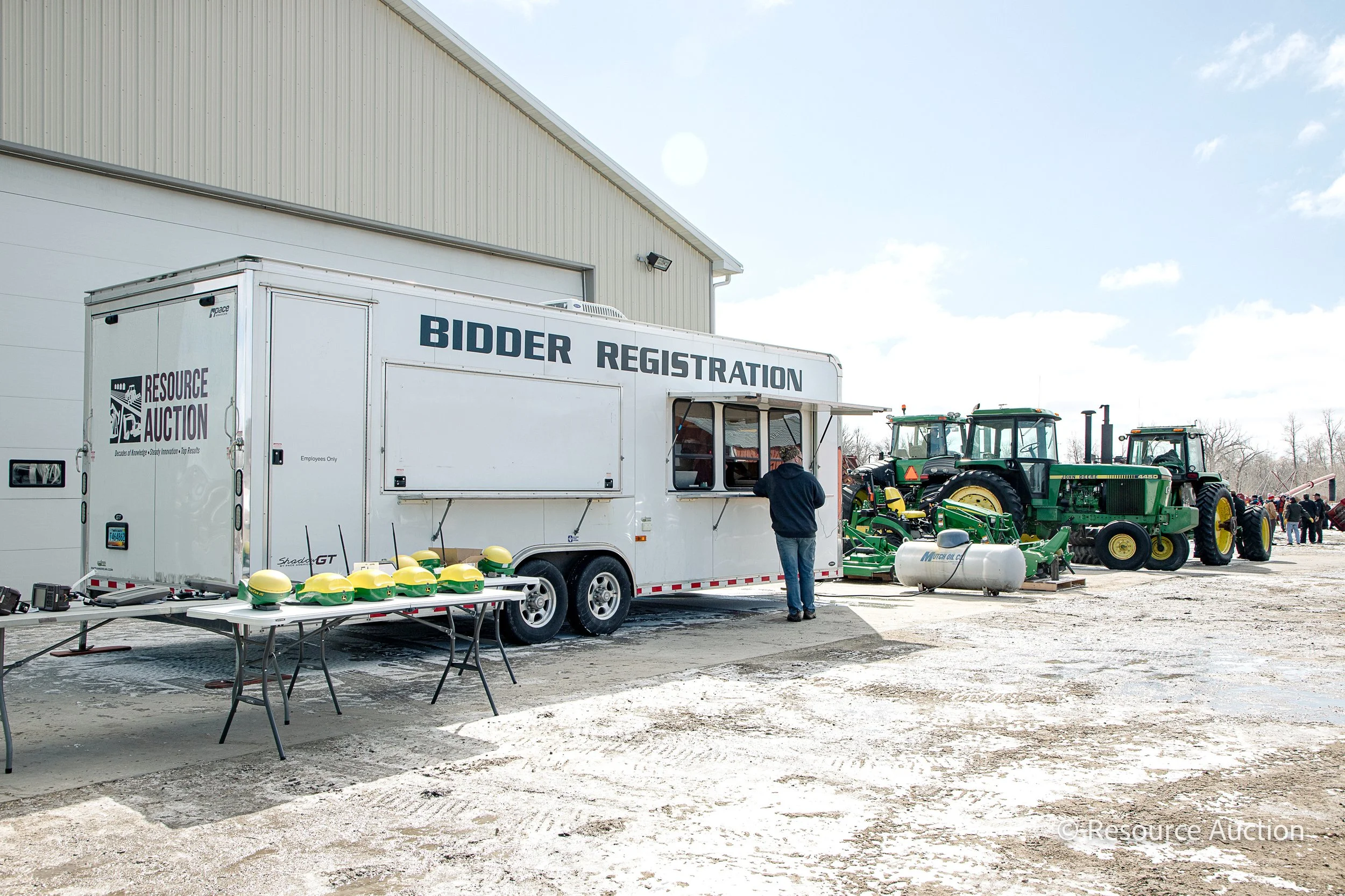 A large, white trailer parked in front of several tractors in the distance. The trailer has "Bidder Registration" on it.