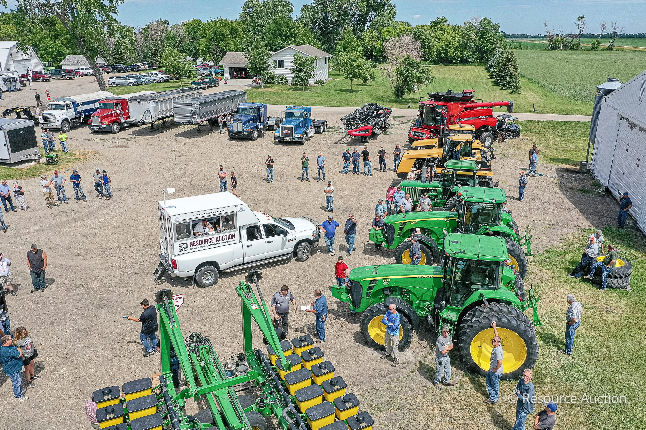 A gathering of farmers all coming together for a machinery auction. There are multiple tractors parked in a line.