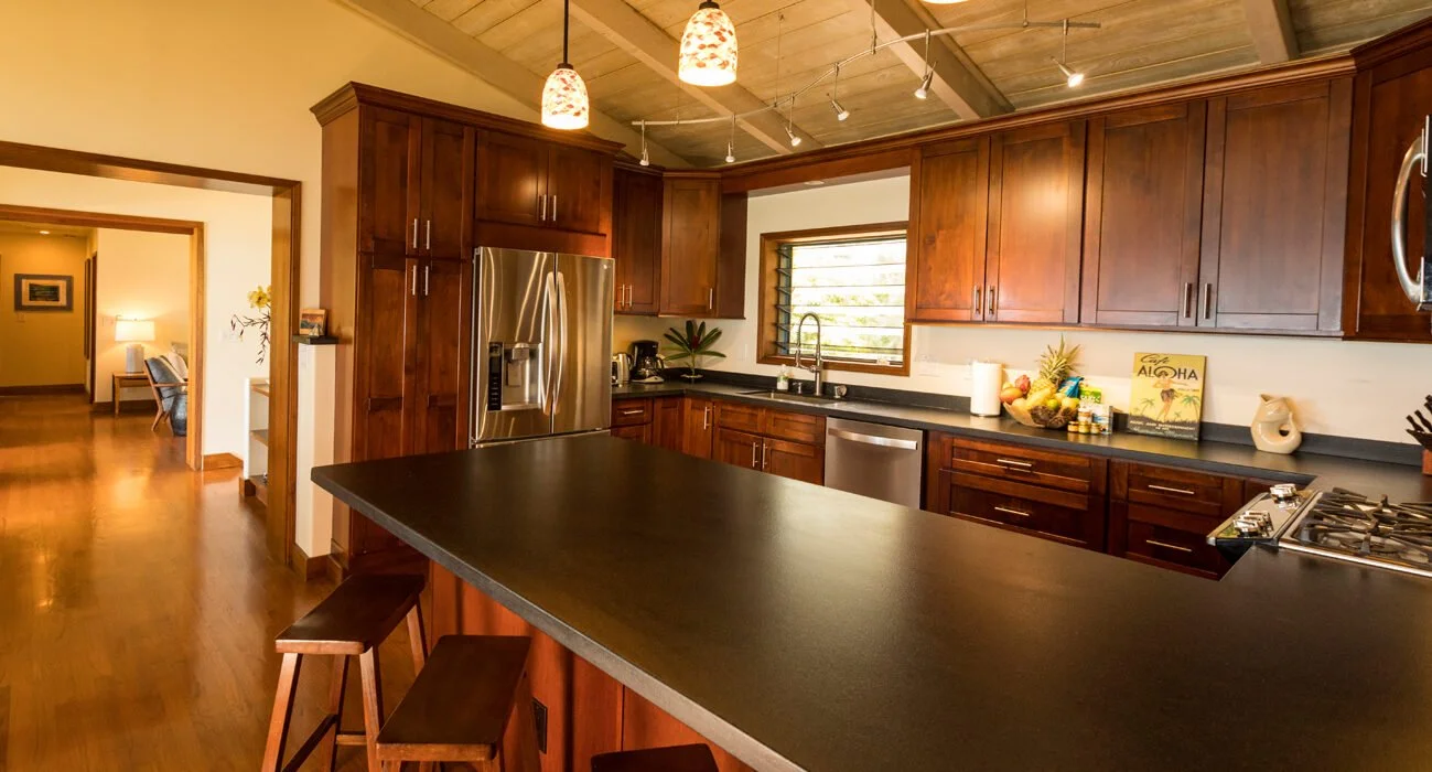 Modern kitchen with wooden cabinets, black countertops, stainless steel appliances, ceiling lighting, and a small island with bar stools.
