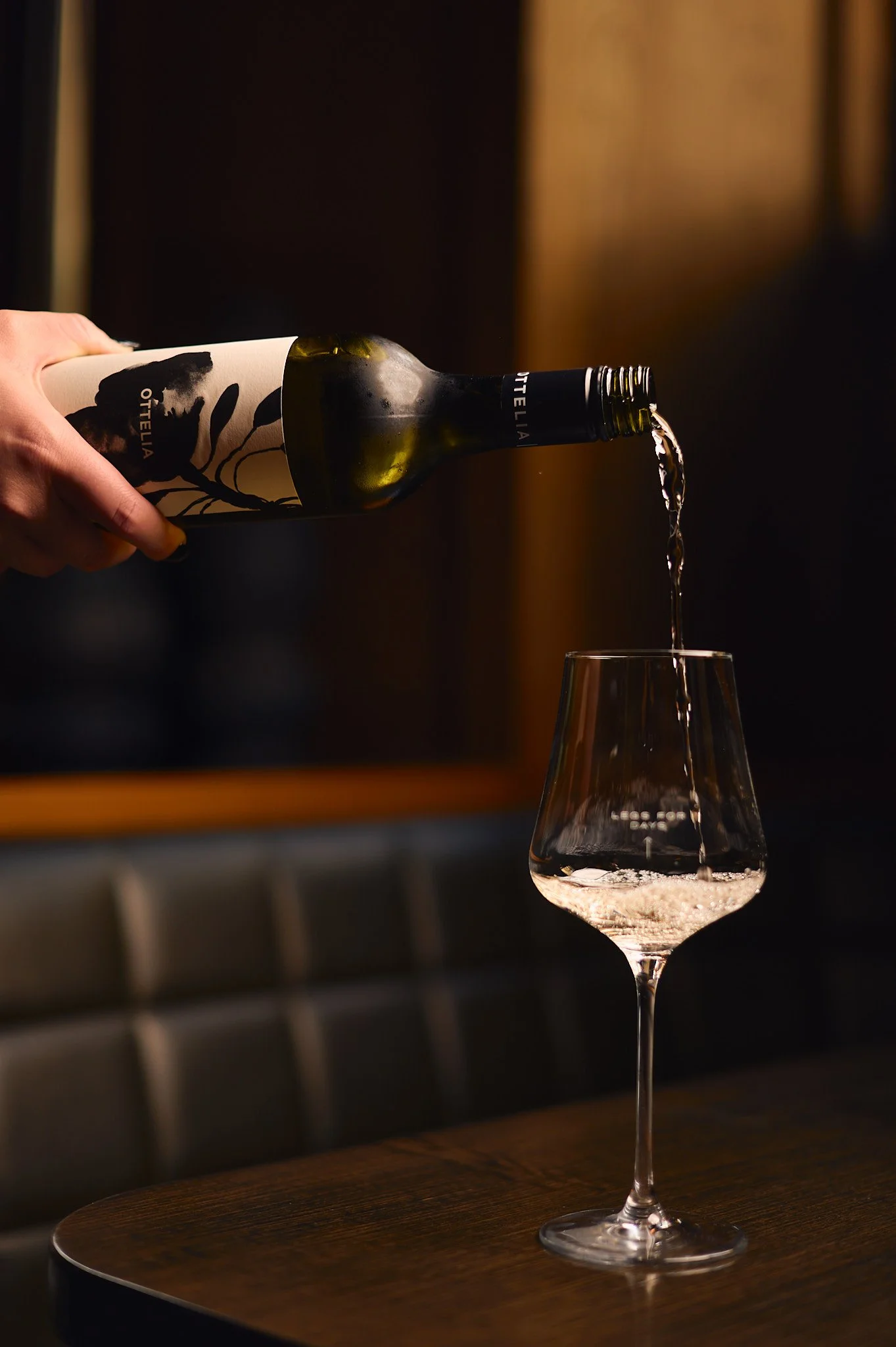 Server is pouring white wine into a wine glass on a wooden table at Angus & Bon.