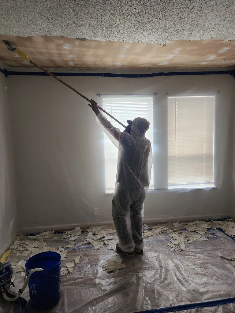 Worker in protective coveralls scraping a damaged ceiling during room renovation