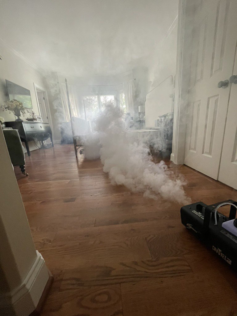 Fog machine releasing thick white smoke across a hardwood-floored room