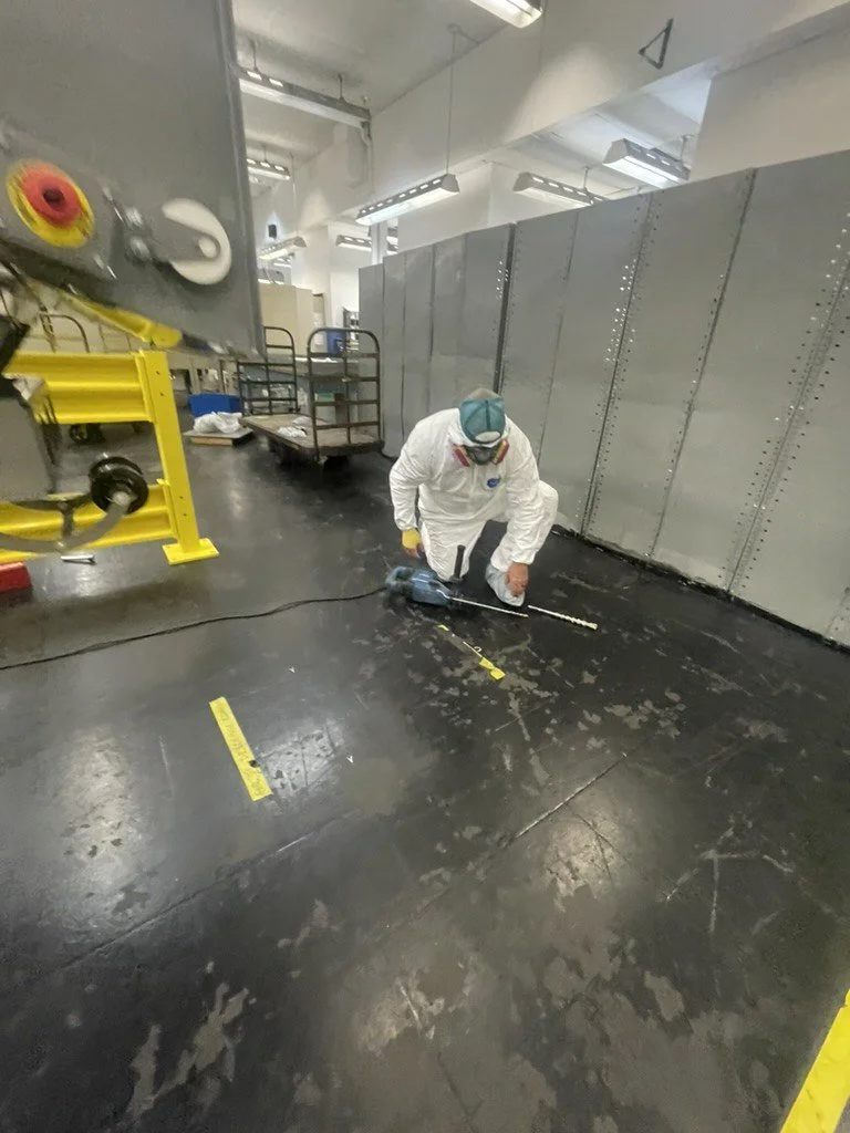 Worker in a white protective suit and respirator kneeling on the floor inside an industrial facility