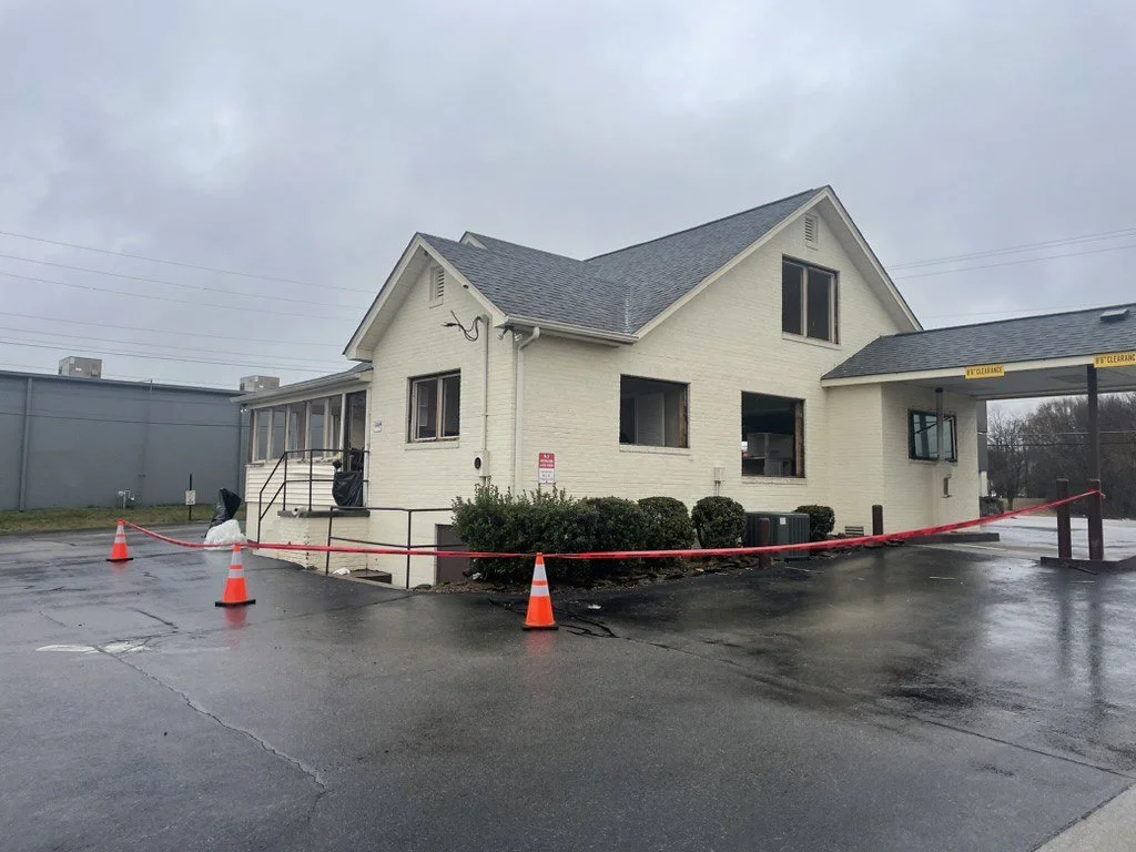 Cream brick building with drive-through canopy, red caution tape, and orange traffic cones on a rainy day