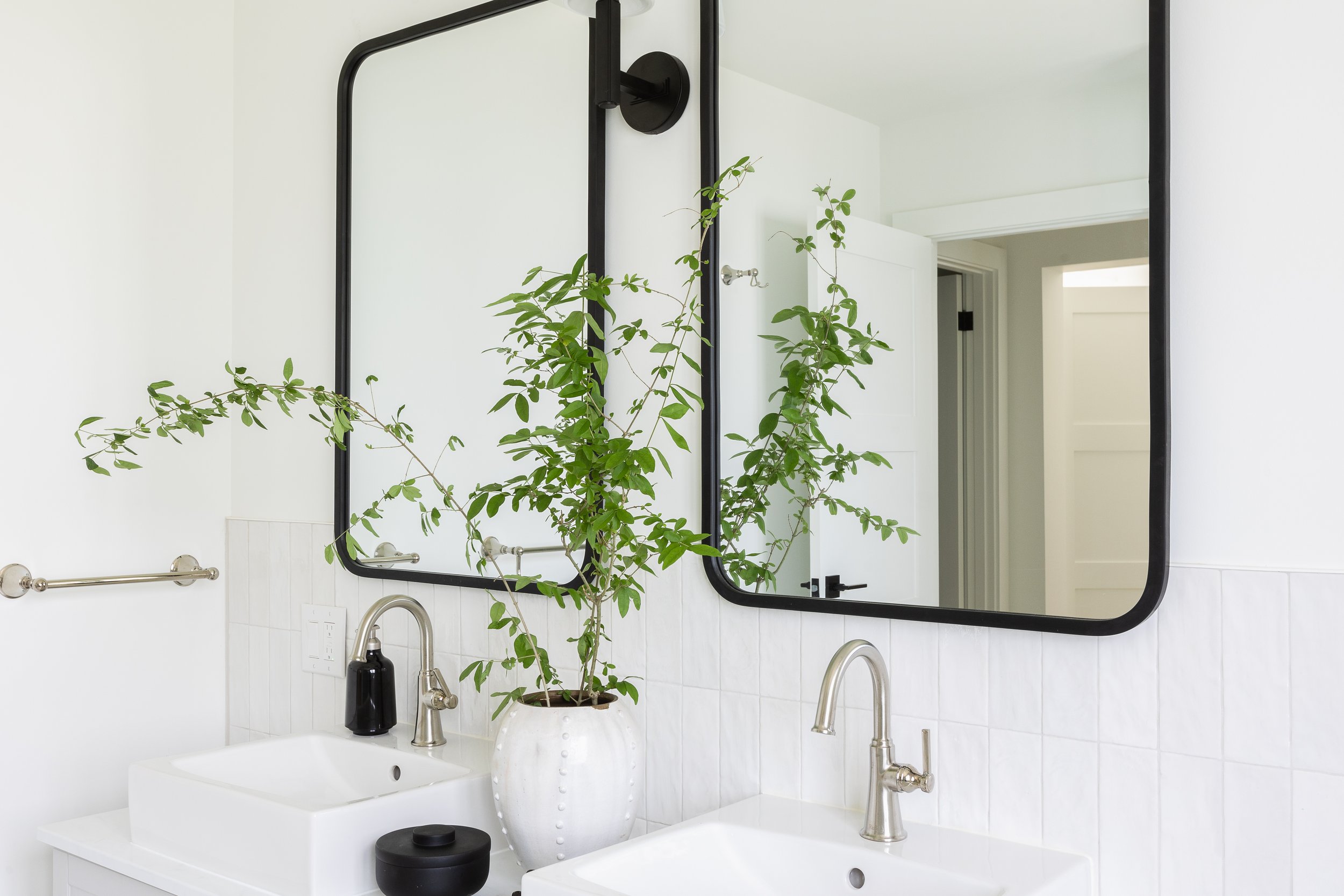 Modern bathroom with a double sink, tall mirrors, and a potted plant on the countertop.
