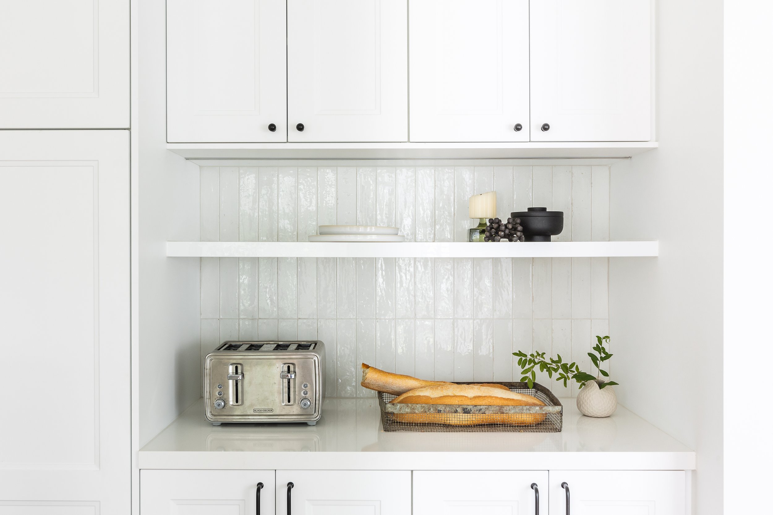 Minimalist white kitchen with a stainless steel toaster, two baguettes on a tray, and potted plant on the countertop.
