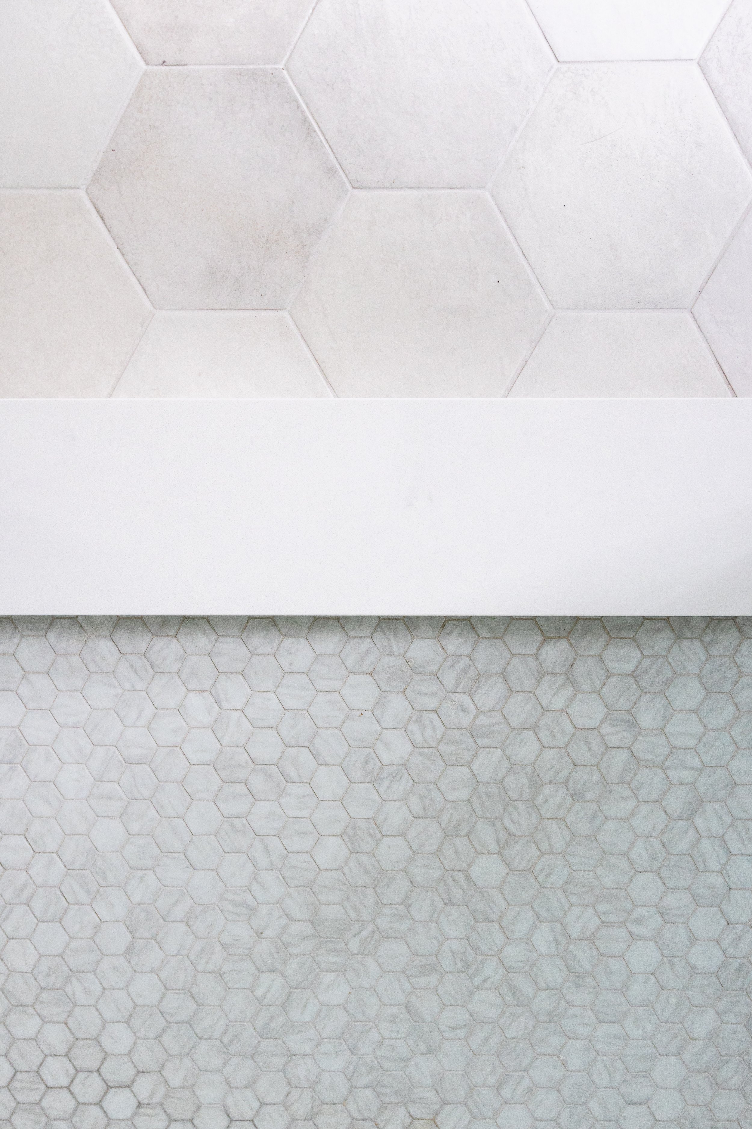 White hexagonal tiles on wall and smaller gray hexagonal tiles on floor separated by a white strip.