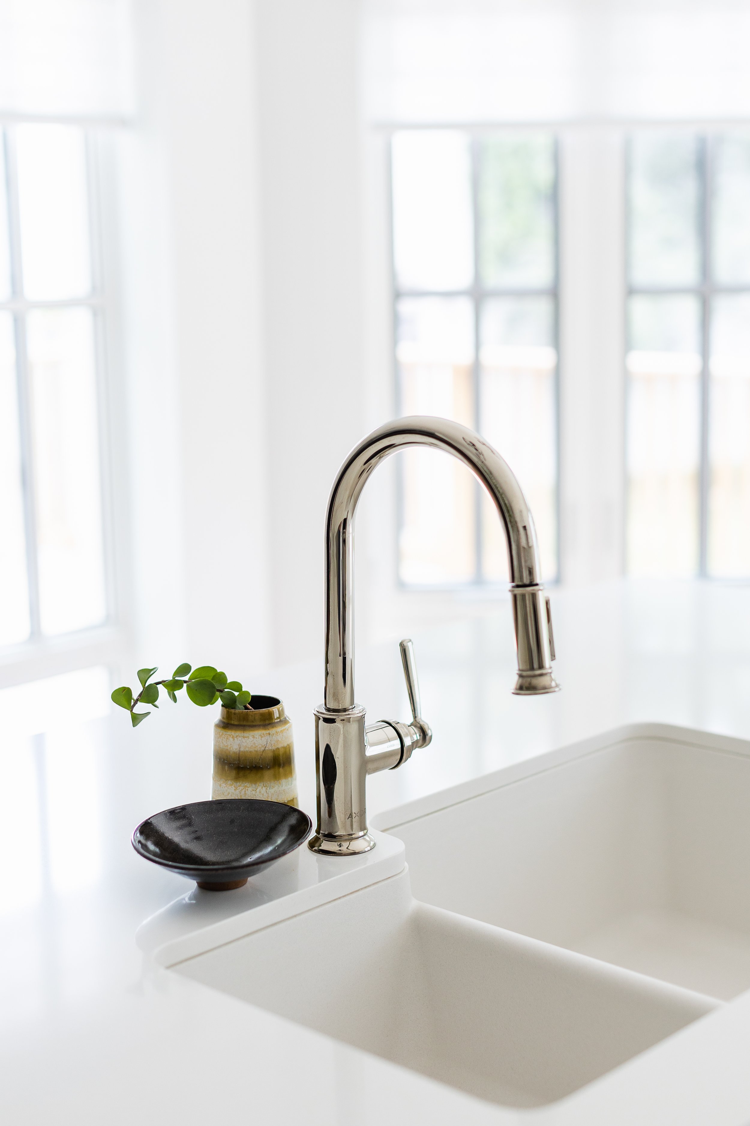 Modern kitchen sink with chrome faucet, black dish, and small vase with greenery.