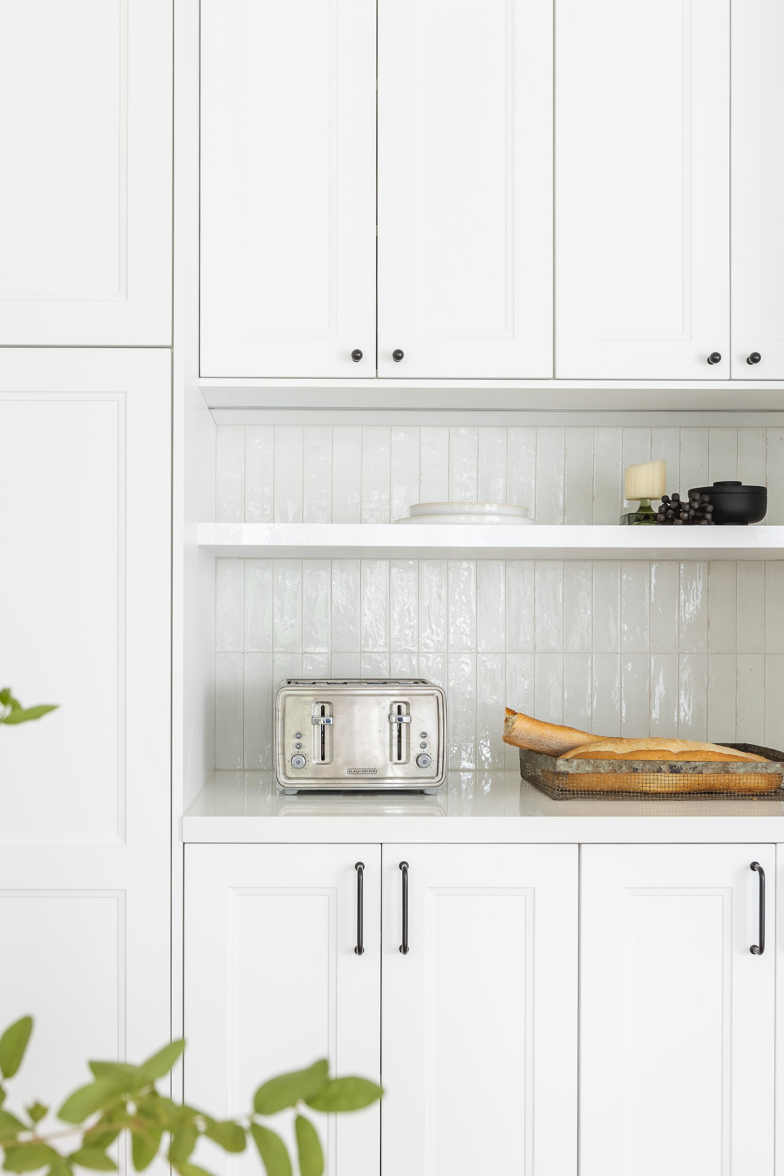 Modern white kitchen with cabinets, a metallic toaster, and a baguette on a tray