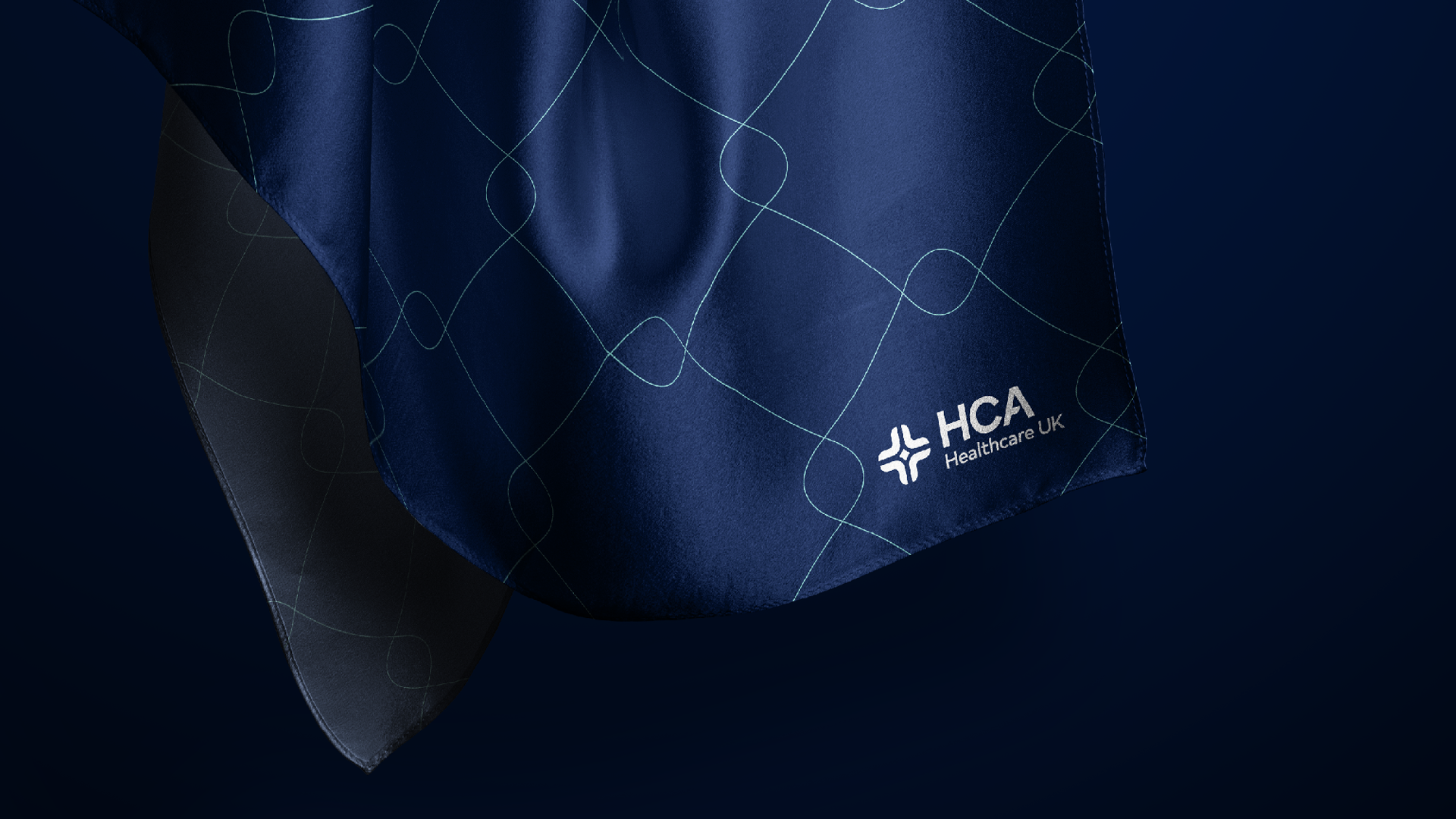 Close-up of blue medical scrubs with light line pattern, displaying the Healthcare UK logo on the lower right corner.