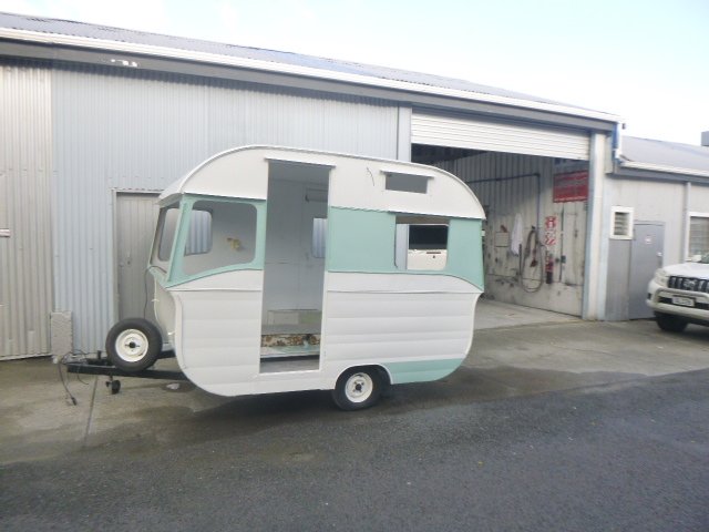 Vintage caravan in light blue and white parked outside a warehouse