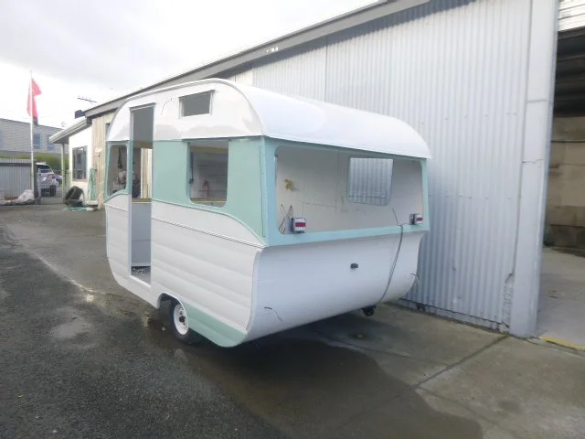 Vintage caravan parked outside a metal building