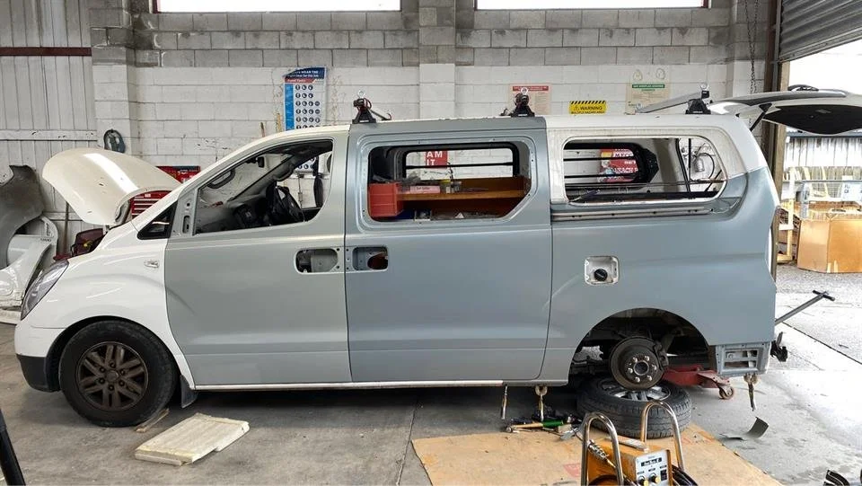 Vehicle under repair in auto body shop, missing side panels and rear wheel, interior exposed.