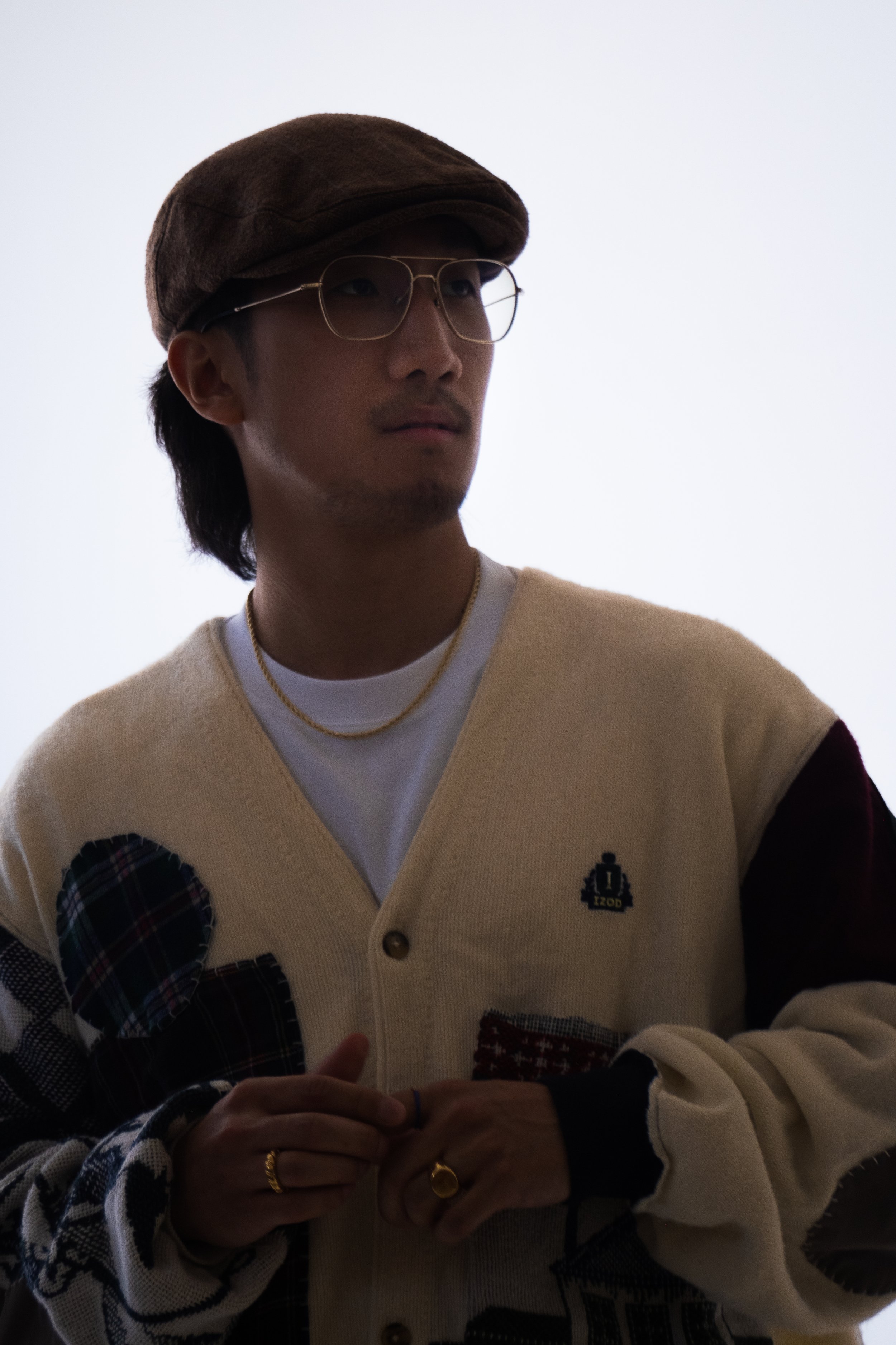 Person wearing glasses and a flat cap, dressed in a patterned cardigan with a logo.