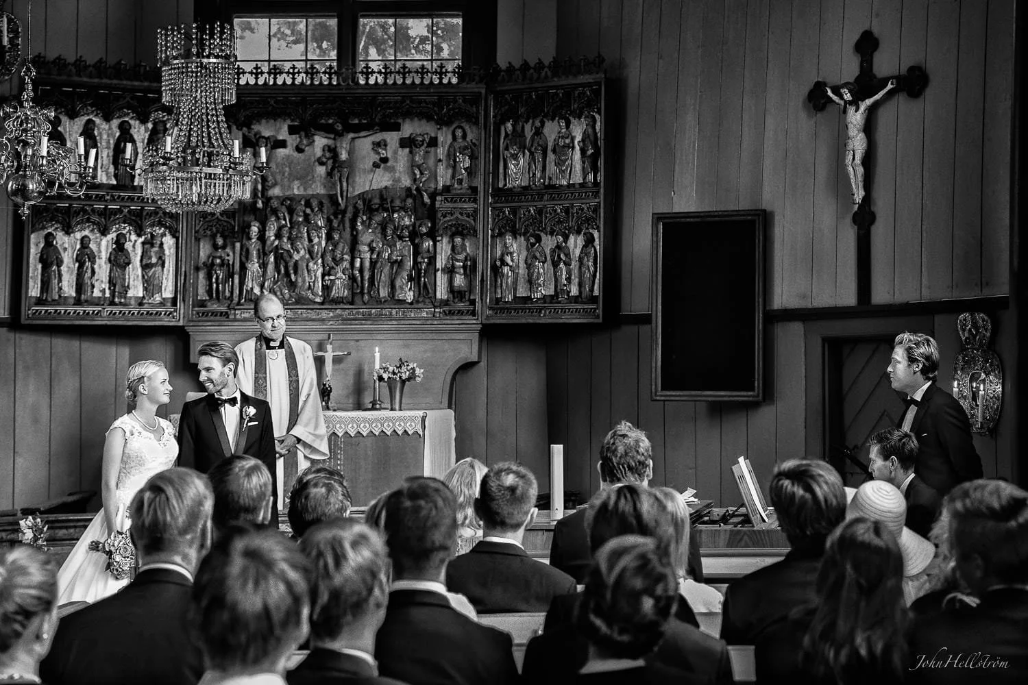 Prisvinnande journalistisk bild av John Hellström, under ett ögonblick där bröllopsparet tittar på varandra under en sång i kyrkan.

Bröllopsceremoni i en kyrka med flera gäster, präster och ett par som gifter sig. Svartvit bild.