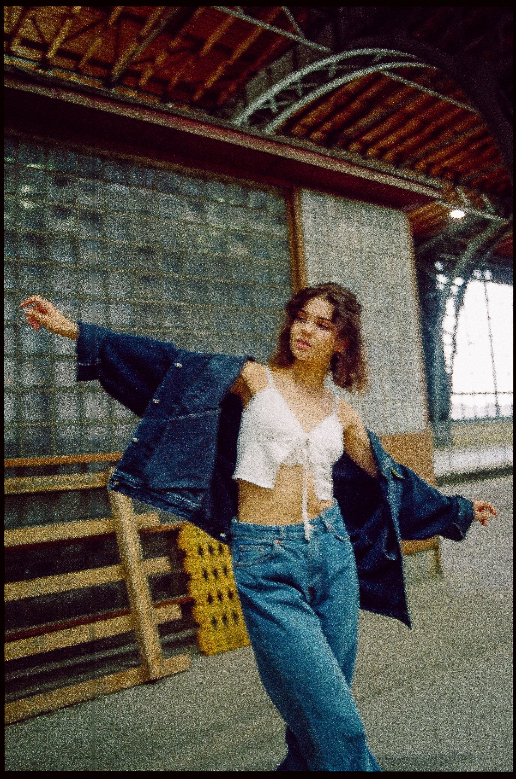 Junge Frau in Jeans, leichtem Top und Jacke, tanzt in einer Industriehalle.