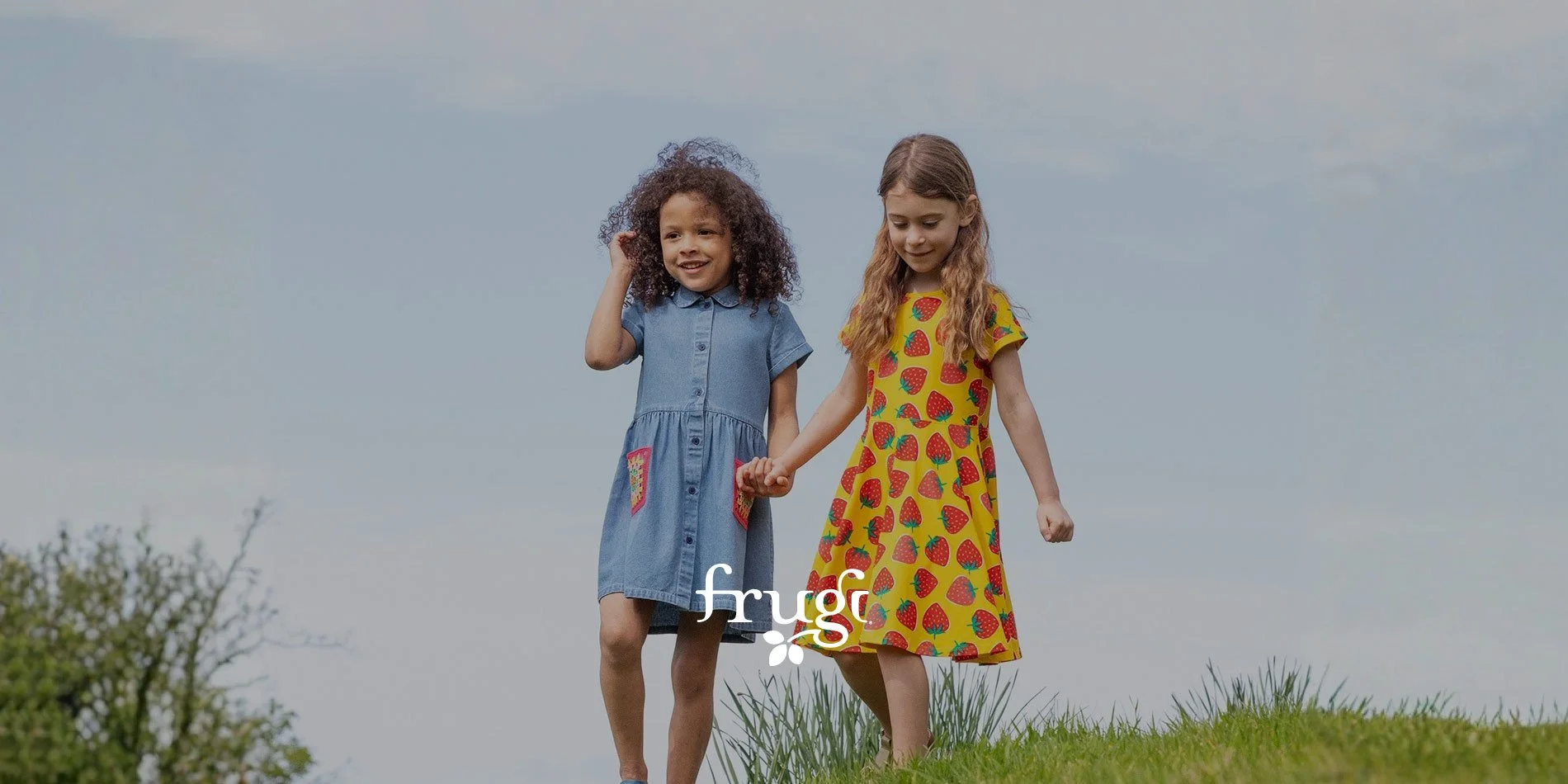 Two children walking in a field and wearing brightly coloured dresses