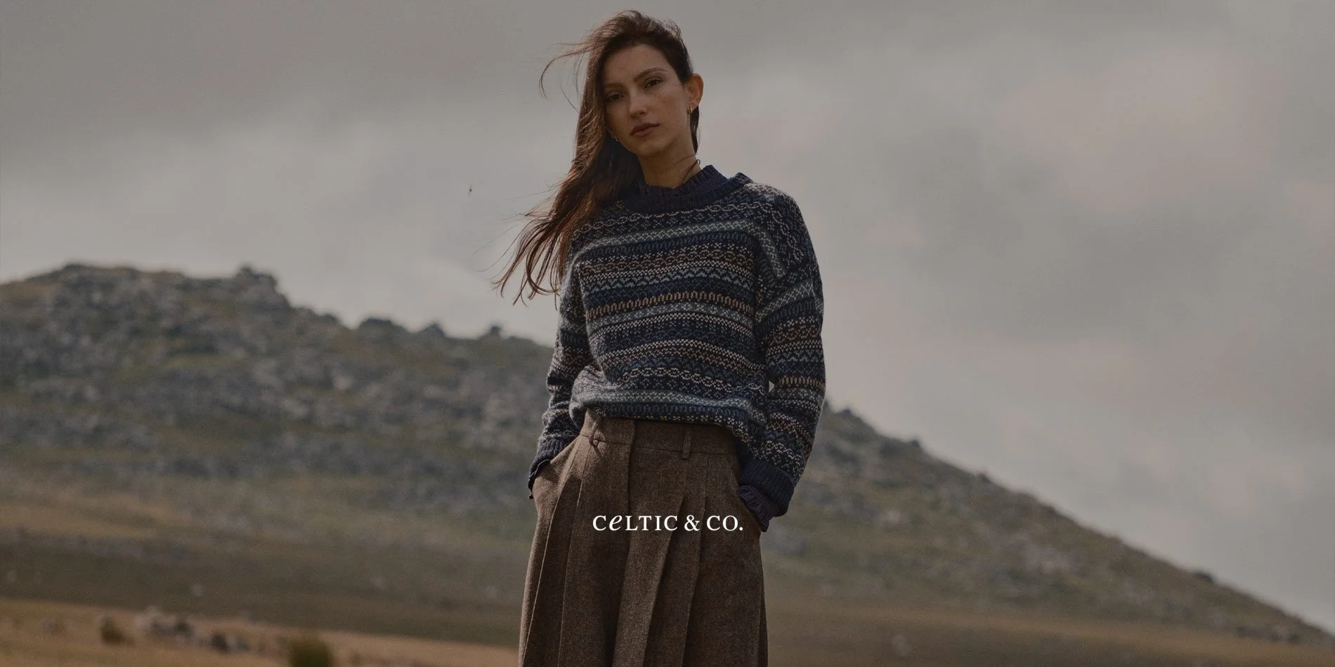 A woman wearing a forest green cashmere jumper and grey beanie, overlaid with the Celtic & Co logo