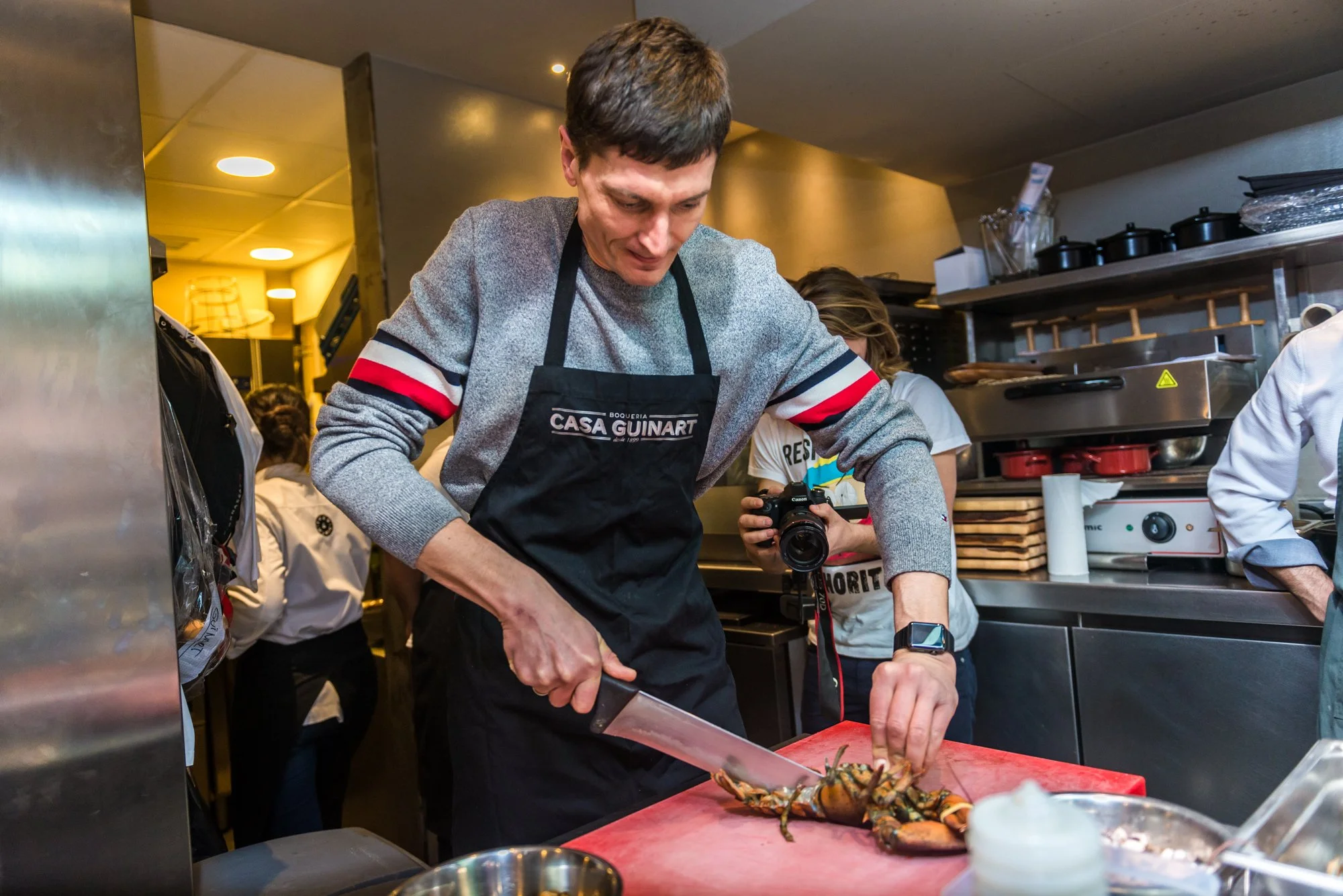 Persona cocinando langosta en una cocina profesional, usando un cuchillo y un delantal que dice "Casa Guinart".