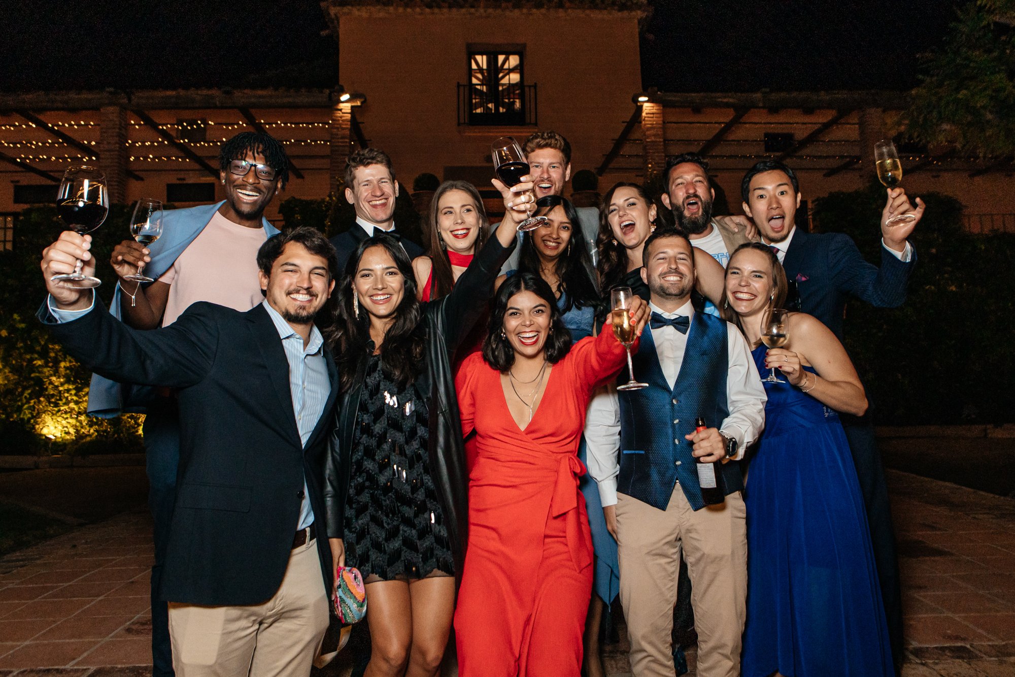 Grupo de personas celebrando con copas de vino, vestidos de manera elegante en un evento nocturno al aire libre.