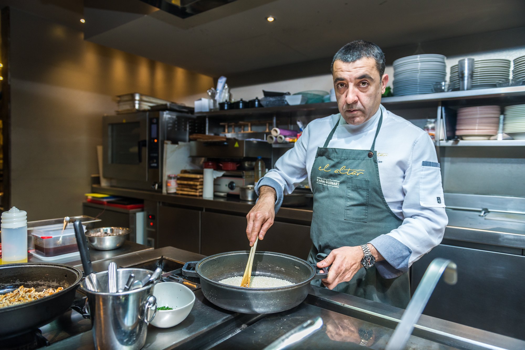Chef cocinando en una cocina profesional, usando una sartén y vistiendo un delantal de cocina verde.